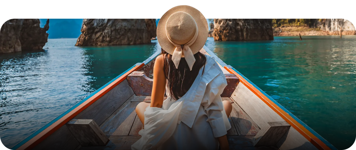 Person sitting at the front of a wooden boat, surrounded by limestone cliffs and turquoise water, symbolizing serene and flexible travel experiences.