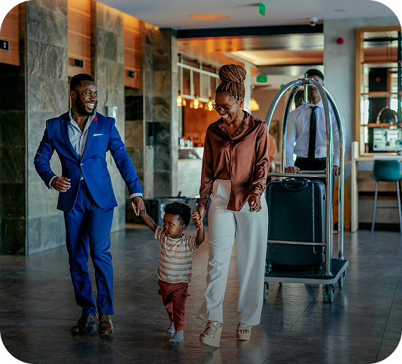 A smiling couple, holding the hands of a small child between them, walk through a hotel lobby