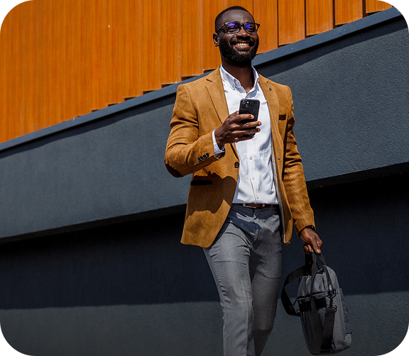 A well dressed man walking confidently outdoors with a phone and bag in hand, reflecting a sense of forward progress