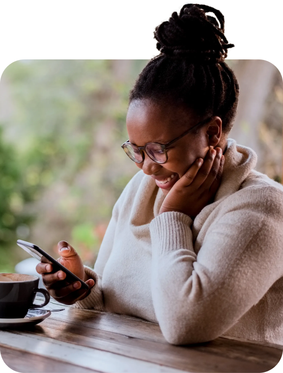 Lady sitting at table smiles while looking down at her smartphone