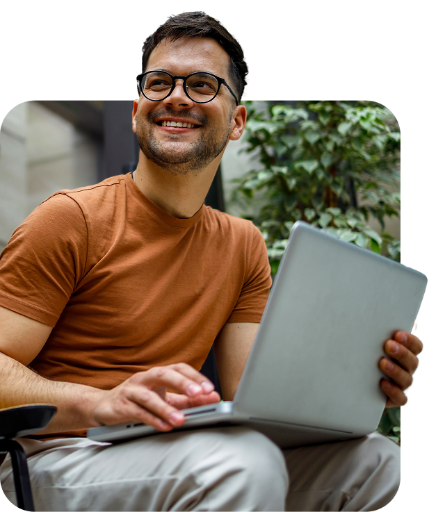 A man using a laptop in a bright indoor space, looking up with a relaxed smile after checking his account activity.
