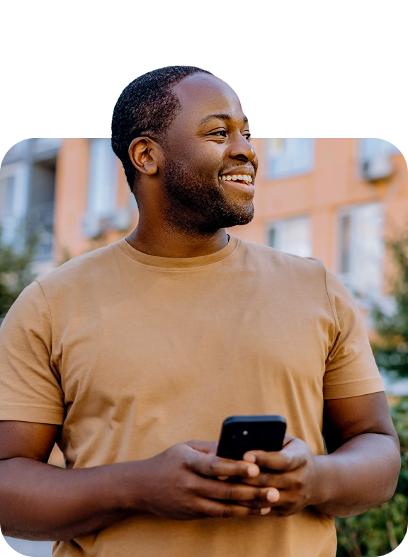 A man standing outdoors, smiling while holding a smartphone, capturing a confident and empowered moment of financial control on the go.
