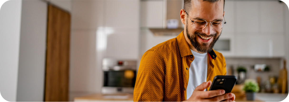 Smiling man checks his phone in the kitchen, enjoying the perks of smart spending.