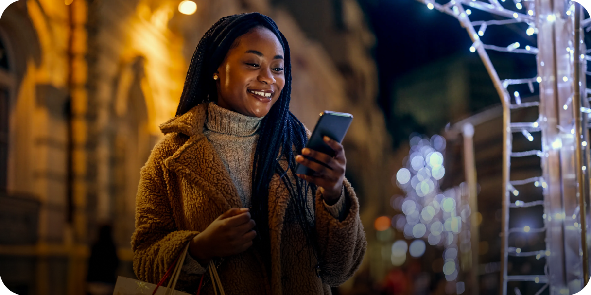 Woman smiling while looking at her phone during an evening shopping trip, suggesting the ease and convenience of managing purchases on the go with a digital payment solution