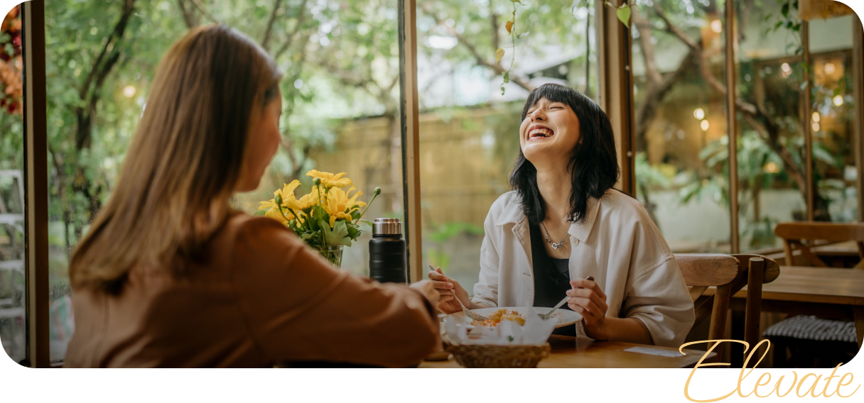 Two people sharing a lighthearted moment over a meal in a bright, relaxed setting—capturing connection, confidence, and clarity.