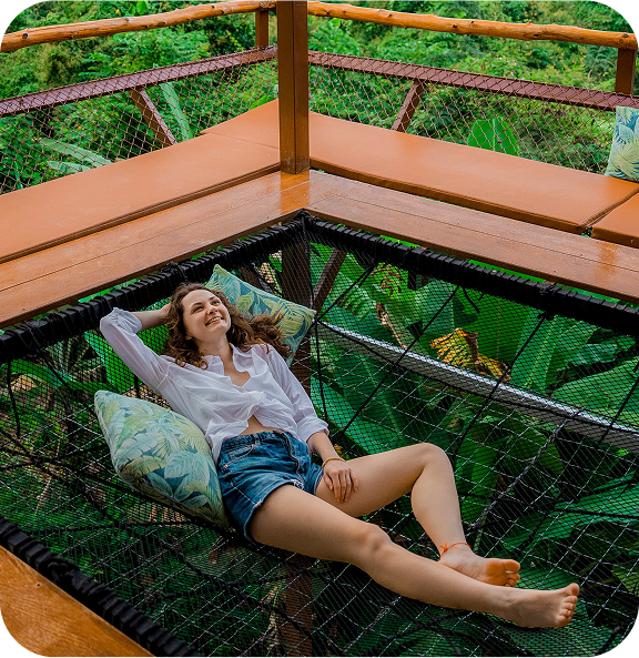Relaxed traveler lying on a suspended net bed with pillows, enjoying a tranquil rainforest setting.