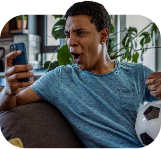 Young man reacting with excitement while looking at his phone, seated in a bright modern living space.