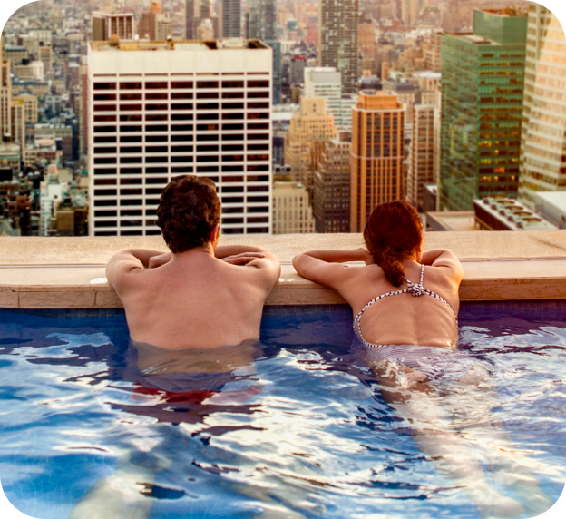 Two people relaxing in an infinity pool above a cityscape with iconic skyscraper