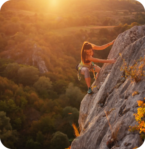 A person rock climbing at sunset against a vast mountain forest backdrop, symbolizing independence and adventurous travel experiences.