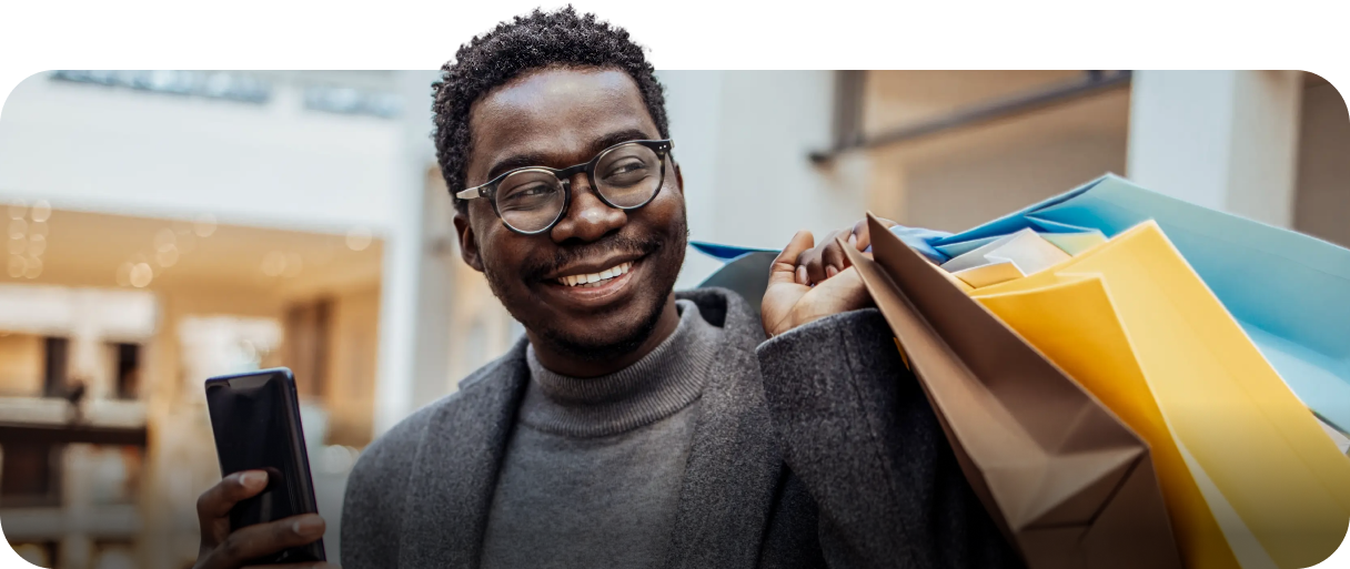 Smiling man holding shopping bags and a smartphone in a mall, representing confidence and ease
