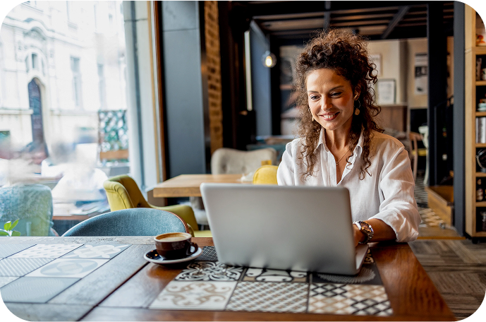 Woman engaged with her laptop in a relaxed cafe setting, a coffee cup sits nearby